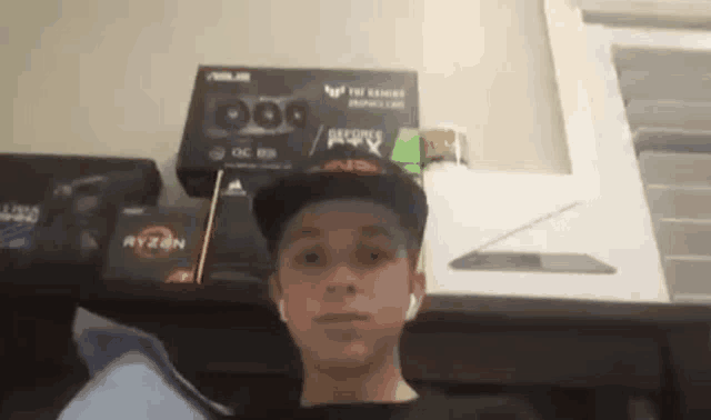 a young boy wearing a hat and ear buds is standing in front of a shelf with boxes on it .