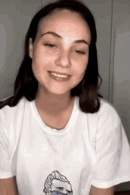 a woman wearing a white t-shirt with a drawing of a hand on it is smiling