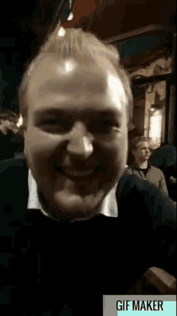 a gif maker shows a man smiling and a woman sitting in the background