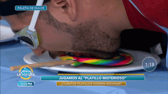 a man eating a colorful lollipop on a plate with the time 1:03 pm on the screen