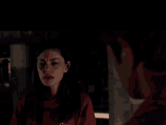 a man and a woman are looking at each other in a dark room . the woman is wearing a red sweatshirt .