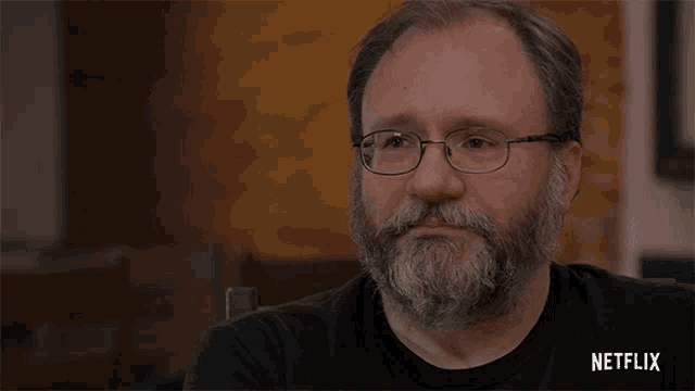 a man with glasses and a beard has a netflix logo on his black shirt