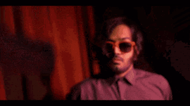 a man wearing sunglasses is holding a gun in his right hand
