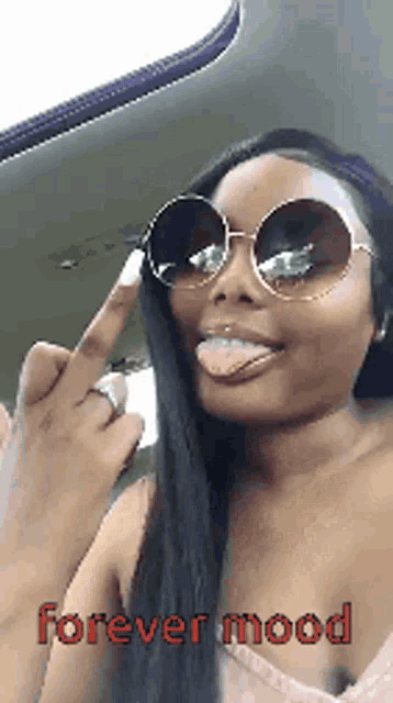 a woman wearing sunglasses is sticking her tongue out and giving the middle finger while sitting in a car .