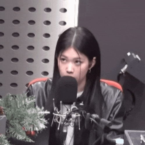 a woman is talking into a microphone with a christmas tree in the background