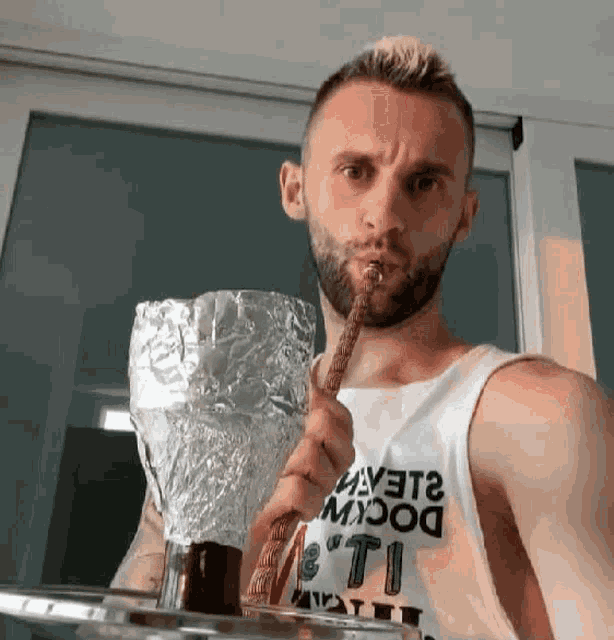 a man with a beard is smoking a hookah while wearing a white tank top that says " yeti " on the front