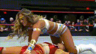 a woman in a wonder woman costume is kneeling over a wrestler in a wrestling ring .