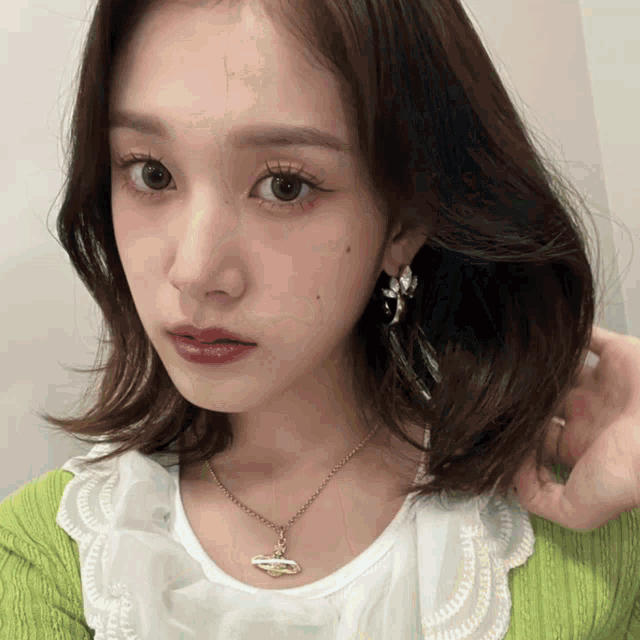 a woman wearing a green sweater and a white shirt has a necklace on her neck