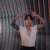 a man in a white shirt is standing in front of a metal wall with his arms up .