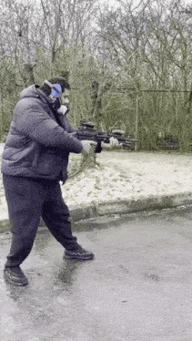 a man in a black jacket is holding a rifle on a street .