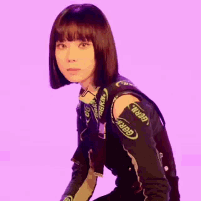 a woman with short hair and bangs is standing in front of a purple background and smiling .