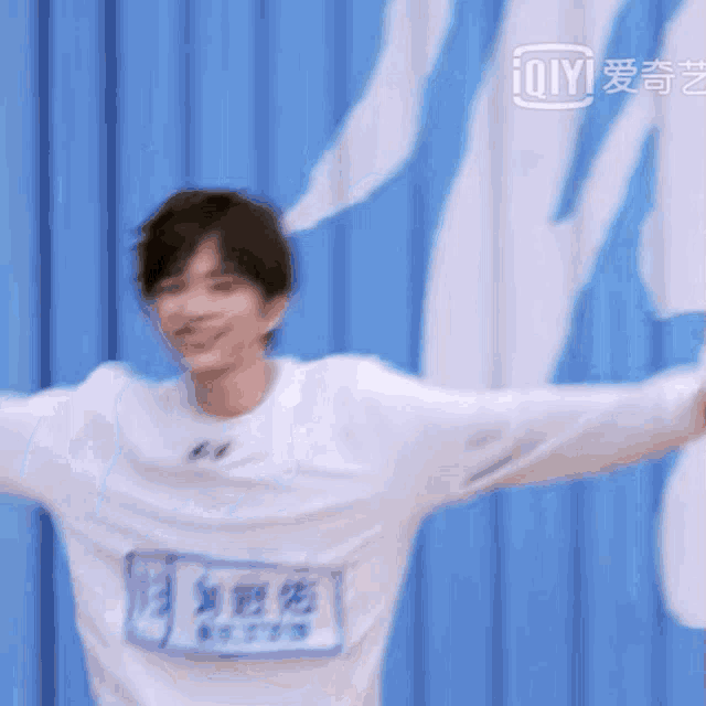 a man in a white shirt is standing in front of a blue wall with his arms outstretched and smiling .
