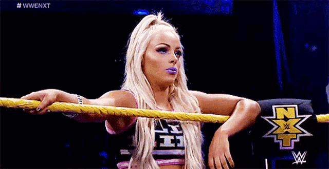 a woman is leaning on a yellow rope in a wrestling ring and looking at the camera .