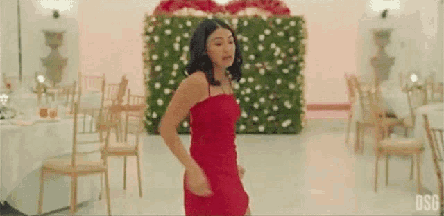 a woman in a red dress is dancing in a room filled with chairs and tables .