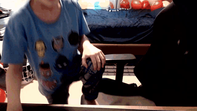 a boy wearing a blue shirt with a cartoon character on it is standing in front of a bed
