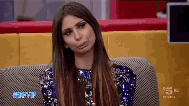 a woman in a blue sequined dress is sitting on a couch with #gfvip written on the screen
