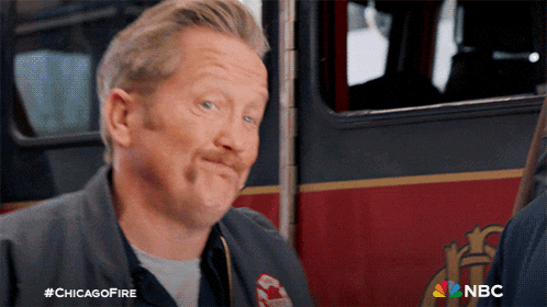 a man with a mustache is sitting in front of a fire truck with nbc written on the bottom