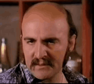 a bald man with a mustache and a beard is making a funny face .