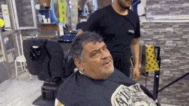 a man is getting his hair cut by a barber wearing a black shirt that says oneil