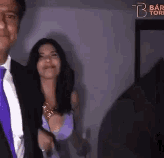 a man and woman are standing next to each other in a room . the woman is wearing a purple dress .