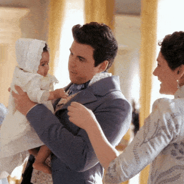 a man in a suit is holding a baby while a woman looks on