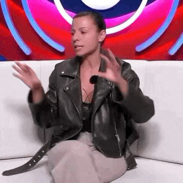 a woman in a leather jacket is sitting on a couch with her hands outstretched .