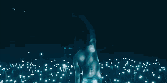 a shirtless man is standing in front of a crowd with a microphone in his hand