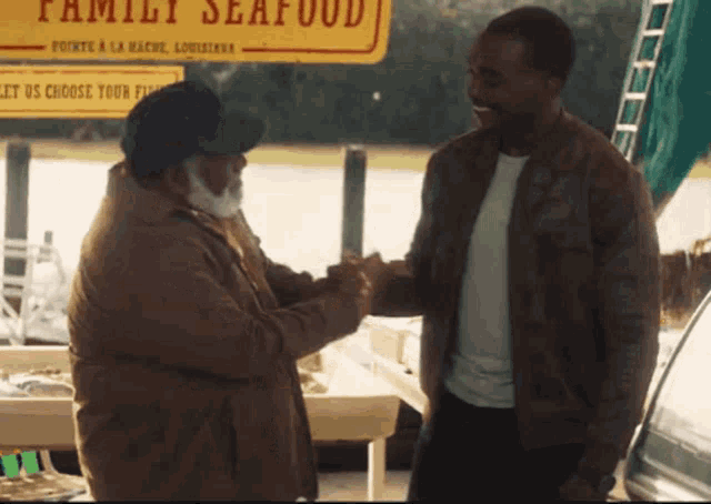 two men are shaking hands in front of a sign that says family seafood