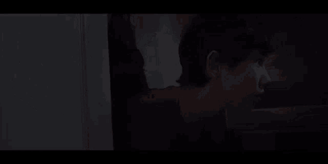 a person is standing in a dark room looking out a window .