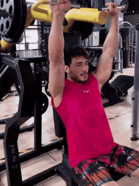 a man in a pink shirt is lifting a barbell in a gym .