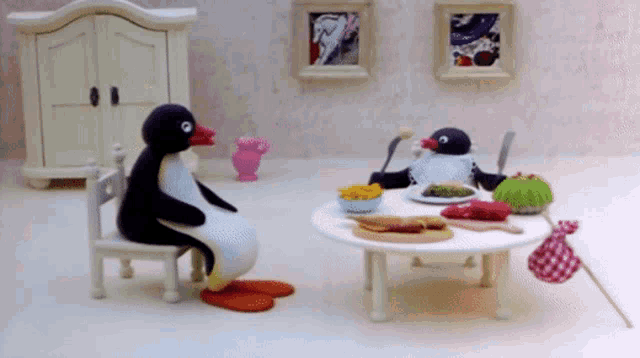 two penguins are sitting at a table with plates of food on it