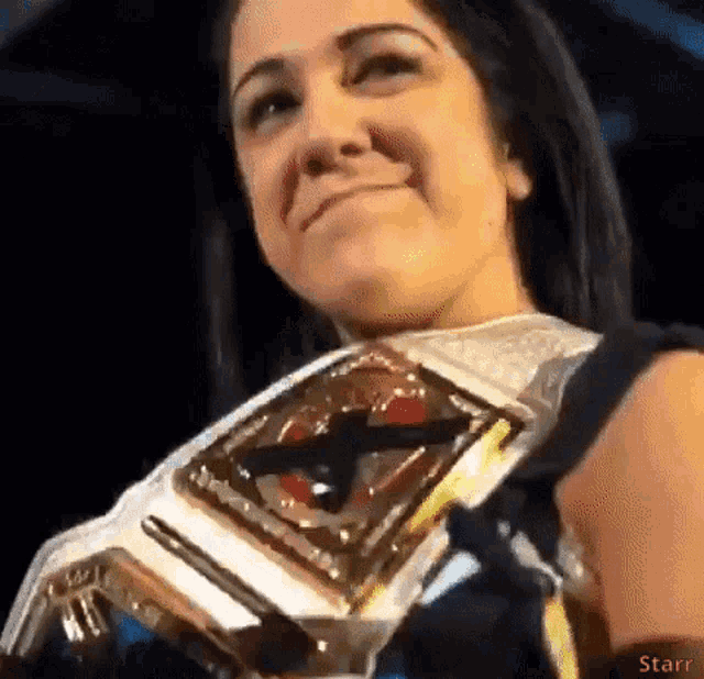a woman is smiling while holding a wrestling championship belt .