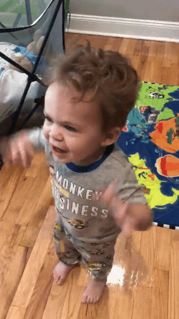 a young boy wearing a monkey business shirt stands on a wooden floor