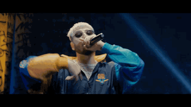 a man wearing sunglasses is singing into a microphone with a jacket that says snr on it