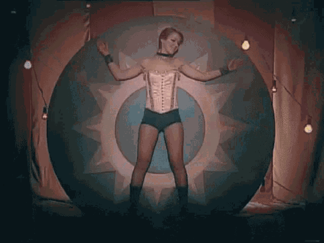 a woman in a corset and shorts is standing in front of a large circle .