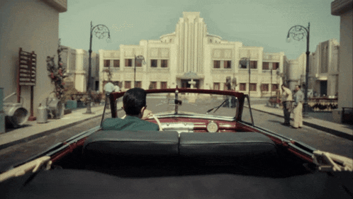 a man is driving a car down a street in front of a building that says ' hotel ' on it