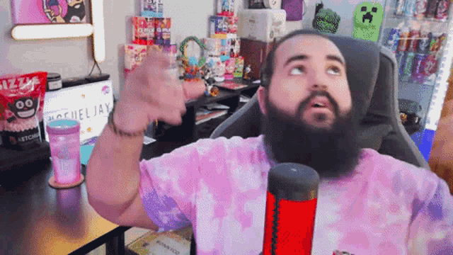 a man with a beard wearing a pink tie dye shirt is sitting at a desk