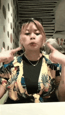 a woman is sitting at a table making a funny face while wearing a floral shirt and sunglasses .