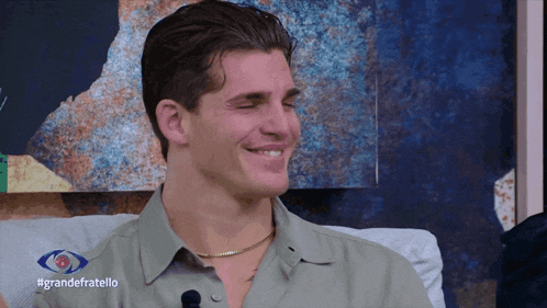 a man sitting on a couch with #grandefratello written on the bottom of his shirt