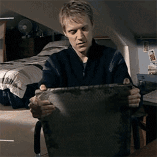 a man in a blue jacket is holding a piece of paper in front of a bed