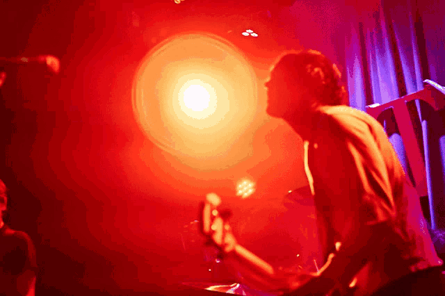 a man playing a guitar in a dark room with a red light in the background