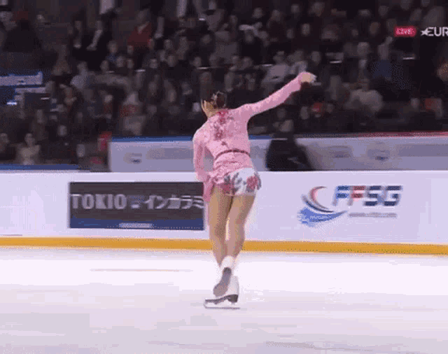 a woman in a pink dress is skating on ice in front of a crowd .
