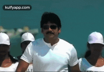 a man wearing sunglasses and a mustache is standing in front of a group of women wearing white hats .