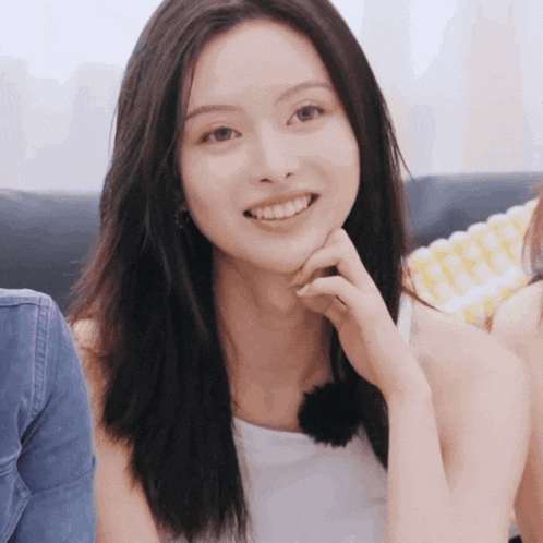 a woman with long black hair is smiling and holding her hand to her chin