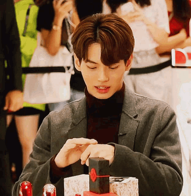 a man in a suit and turtleneck is opening a box with a red heart on it