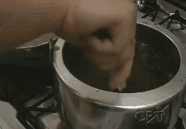 a person is stirring a pot of food on a stove top .