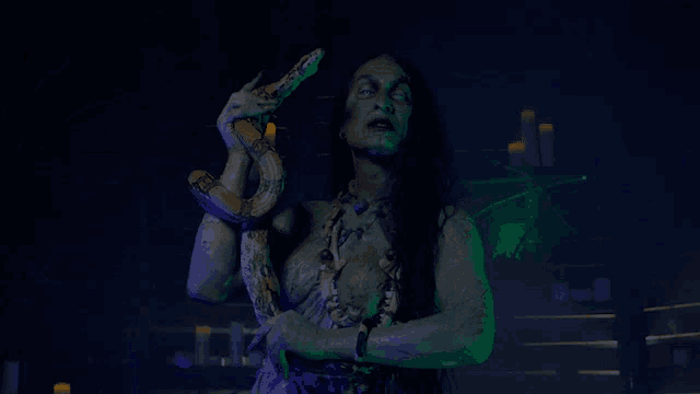 a woman with green paint on her face is holding a snake in her hands