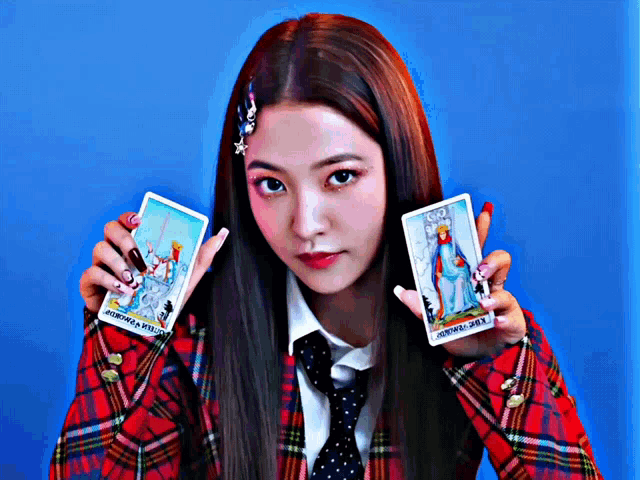 a woman in a plaid shirt and tie is holding two tarot cards one of which says the queen of swords