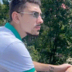 a man wearing glasses and a white shirt with a green collar is sitting in front of trees .