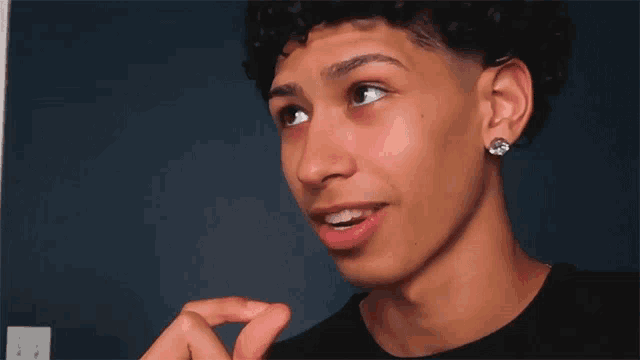 a young man with curly hair is wearing earrings and a black shirt .